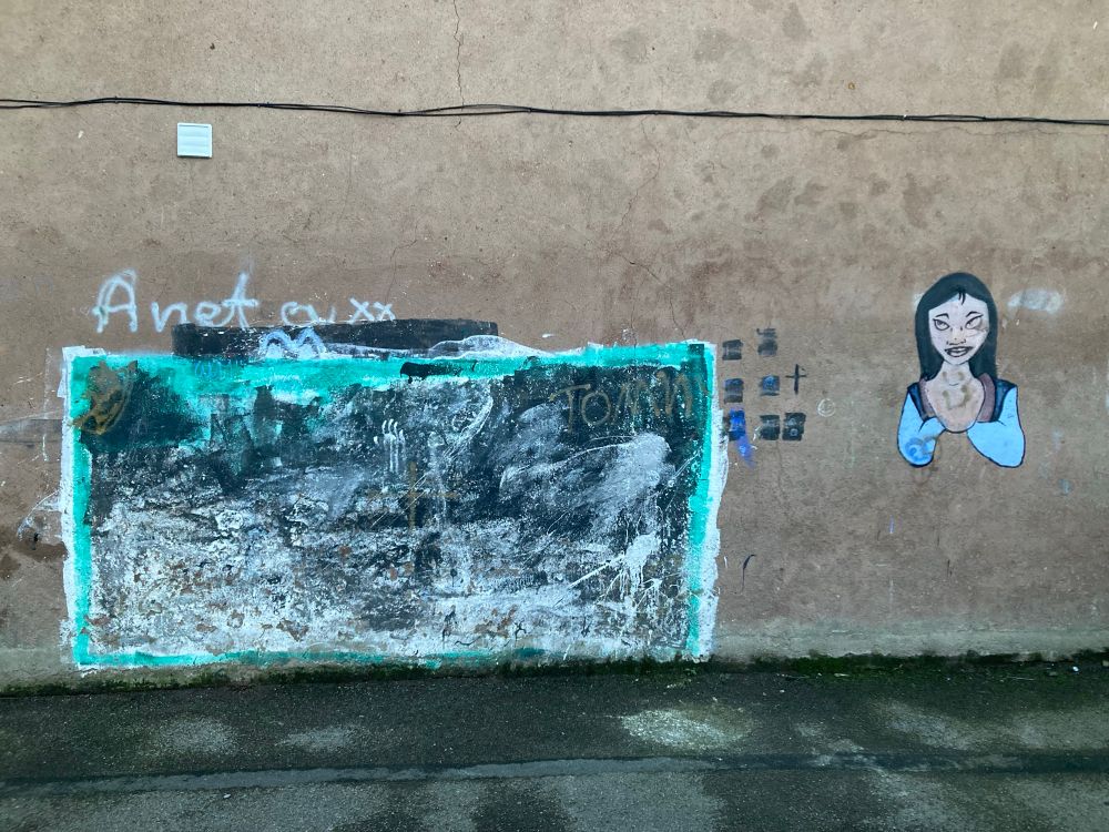 Improvised goal on an end terrace graffitied on the wall in black and green next to a portrait of a woman.