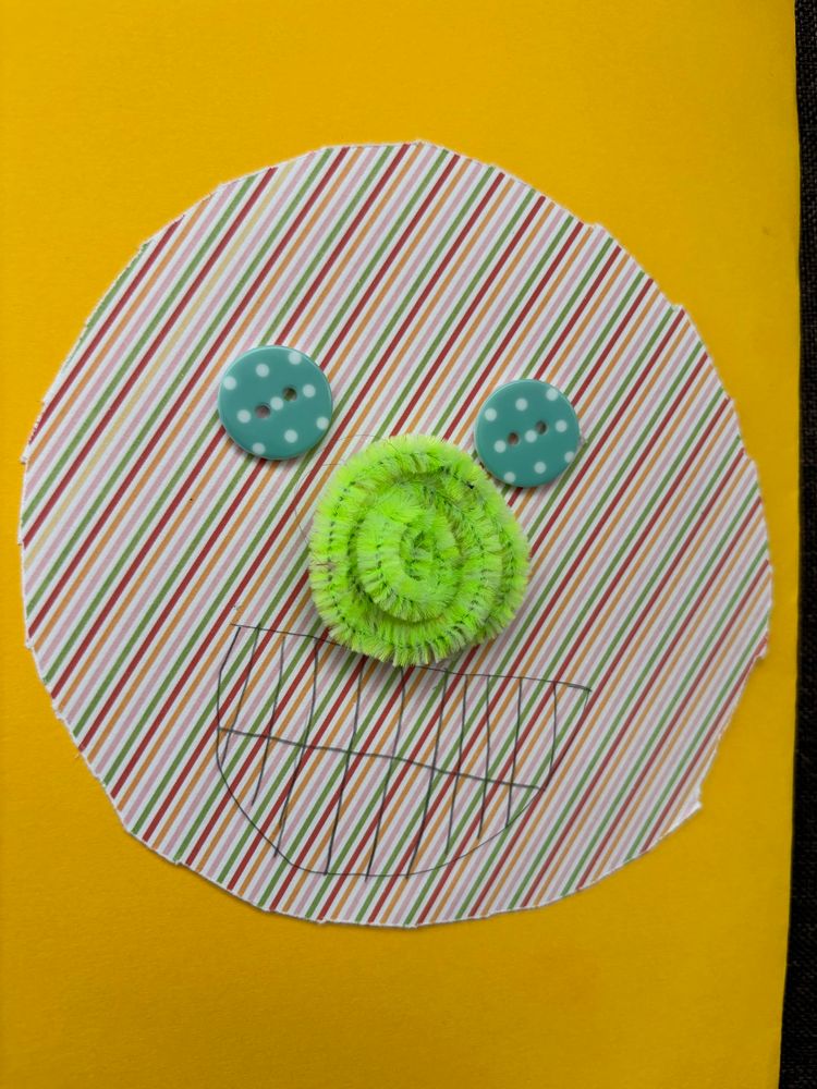 The front of a get well soon card with a portrait of me made from a circle of rainbow striped paper, a spiral of neon green pipe cleaner for a nose, two green buttons with white dots and a mouth drawn on with biro.