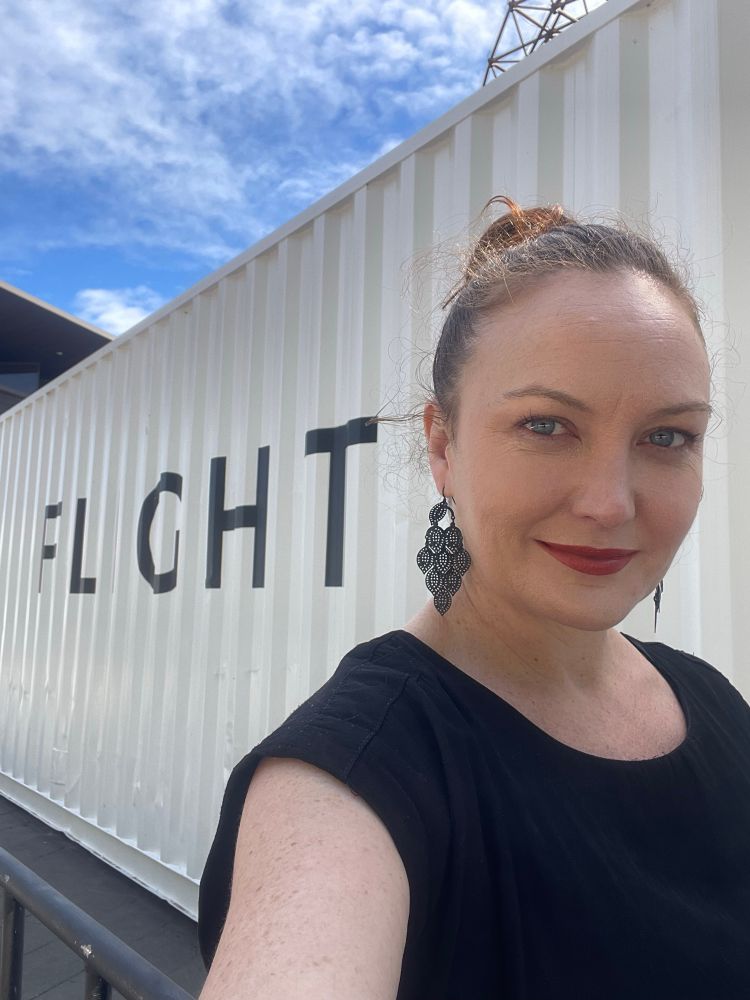 Women stands in front of a White shipping container bearing g the word FLIGHT. 