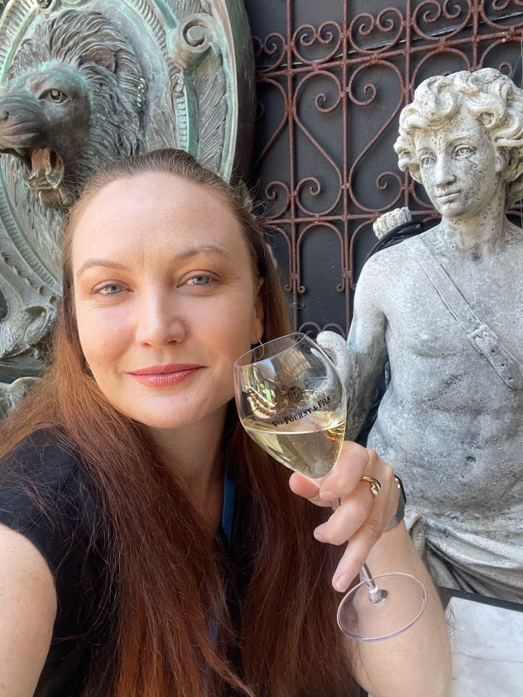 Redhead lady raises a glass of champagne as she drinks next to a marble statue 