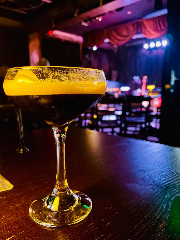 An espresso martini anticipates the music to imminently fill an empty stage filled with instruments. 