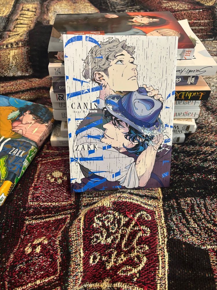 A copy of Canis—Dear Rain by Zakk, prequel to Dear Hatter, featuring the two male leads in an embrace in the rain. 