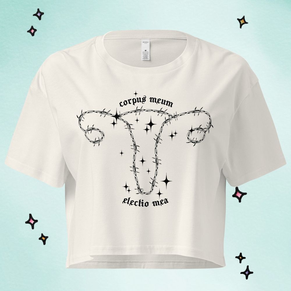 White T-shirt containing artwork of a uterus made of barbed wire, surrounded by sparkles. Features text “corpus meum, electio mea” meaning “my body, my choice” in Latin is featured. 