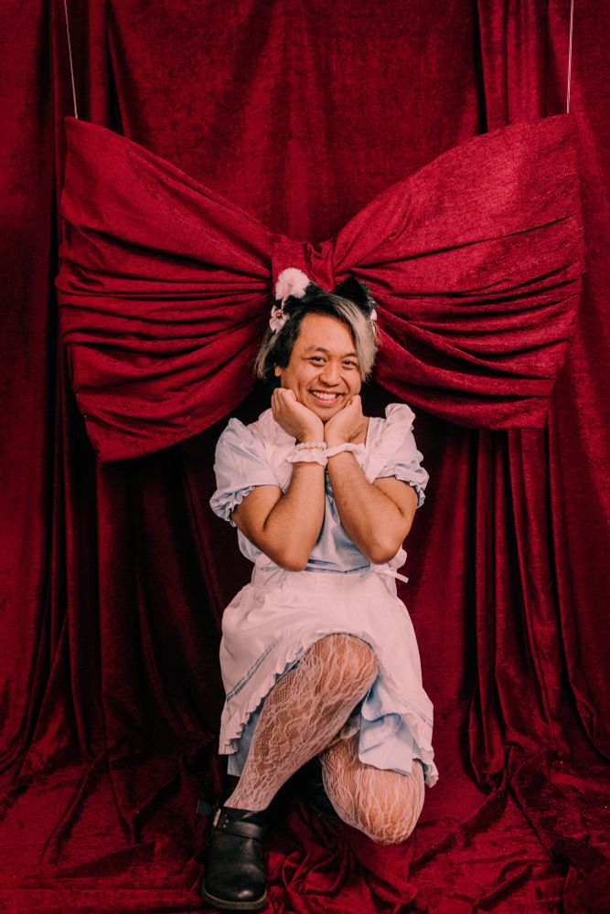 Chris posing wearing cat ears and a light blue maid outfit below a giant bow