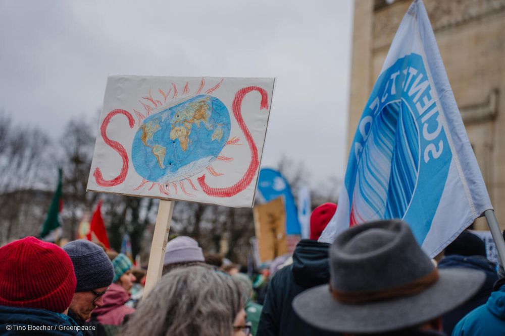 Eine Szene vom Klimastreik in München. Auf einem Schild ist eine brennende Erde zu sehen mit dem Slogan SOS.