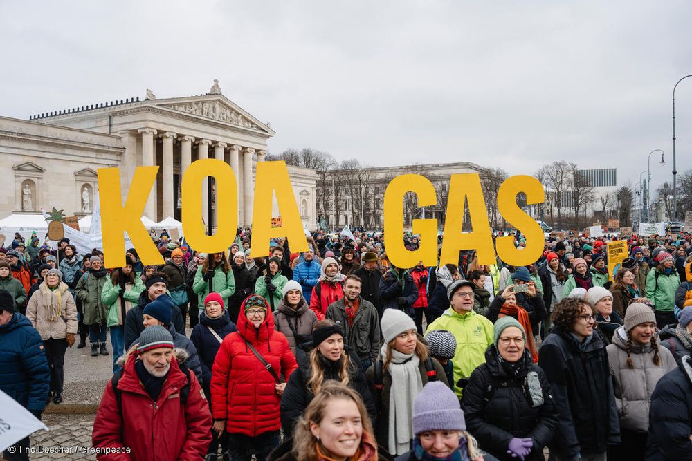 Ein Foto über die versammelten Menschen auf dem Königsplatz in München. Im Mittelpunkt sind Greenpeace-Aktive zu sehen, die einen großen Schriftzug halten mit der Aufschrift: Koa Gas.