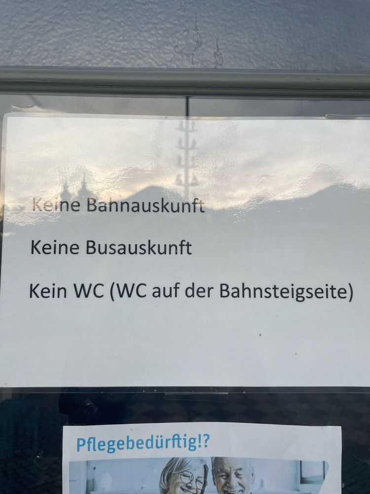 Das Foto zeigt einen Aushang an einem Bahnhof im Chiemgau. Darauf steht: Keine Bahnauskunft, keine Busauskunft, kein WC. Pflegebedürftig?