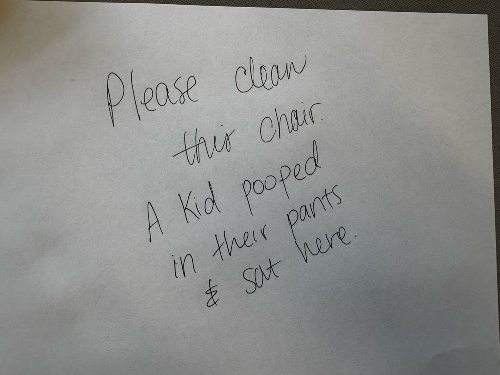 A white piece of paper that says “please clean this chair. A kid pooped in their pants and sat here” 