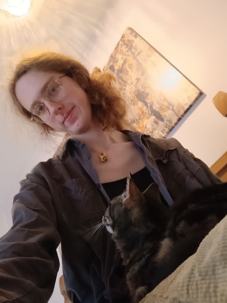 Gwen sits on a bed with a cat lying on her lap staring up at her 