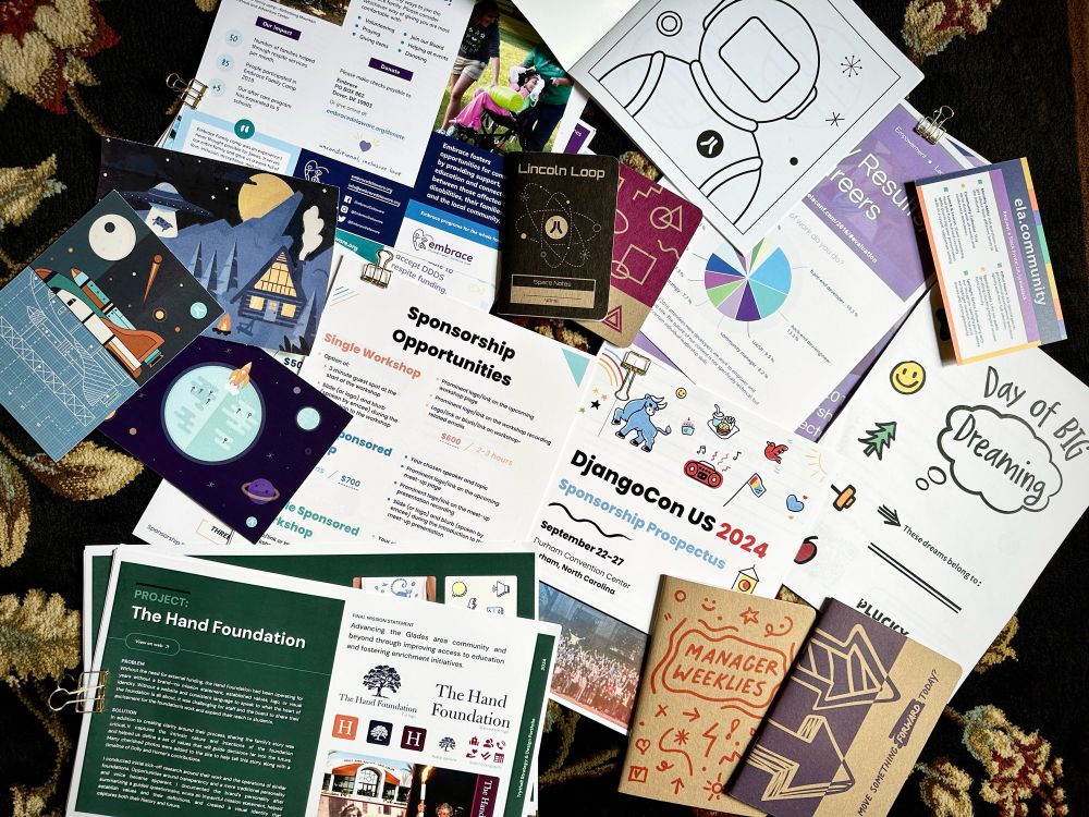 Assortment of print design work scattered on carpet. Work included fundraising materials, notebooks, marketing swag, and cards 