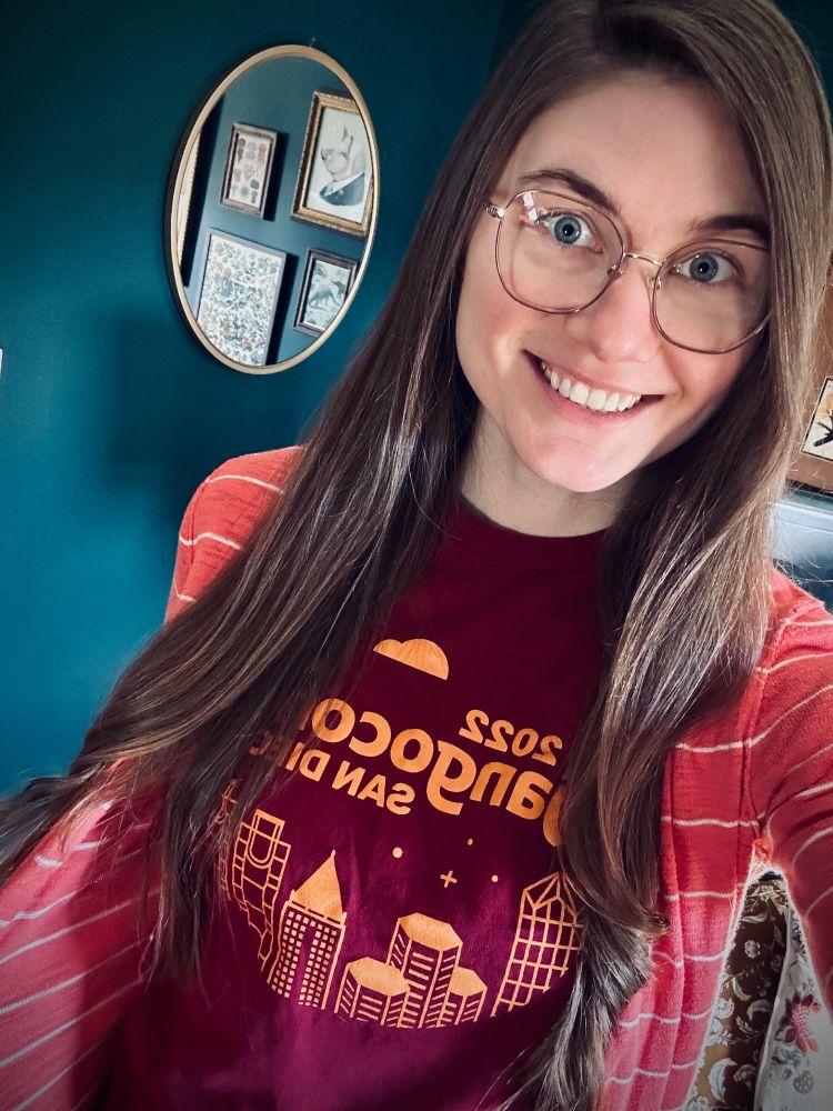 Joni Trythall wearing a maroon DCUS '22 t-shirt with an orange illustrated skyline of San Diego