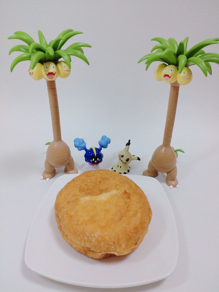 白いラウンドスクエアの皿の上にマラサダが乗っており、皿の奥に左からアローラナッシー、コスモッグ、ミミッキュ、アローラナッシーのモンコレが並んでいるところを撮影した写真。