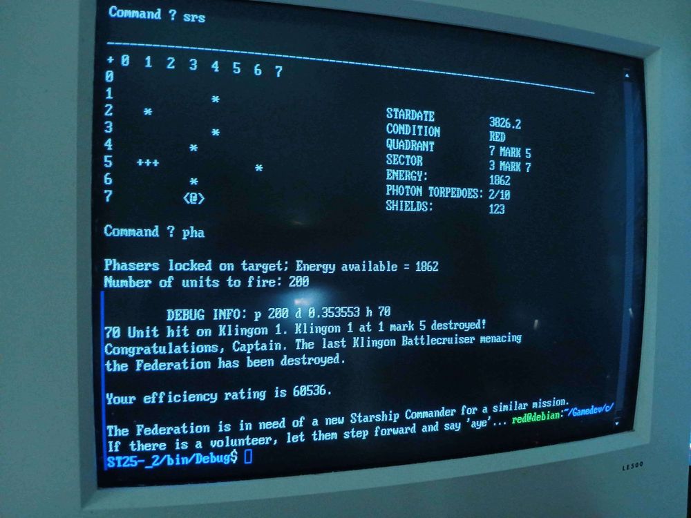 CRT showing a terminal style game which shows a 8x8 grid where stars (asterisks) dot the play area and a Starfleet ship (@) and Klingon ship (three crosses) are fighting. On the right of the map is a status display showing stardate, Red Alert, position, and remaining energy, shields, and torpedoes.

Then text:
Command ? pha
Phasers locked on target; Energy available = 1862
Number of units to fire: 200
DEBUG INFO: p 200 d 0.353553 h 70
70 unit hit on Klingon 1. Klingon 1 at 1 mark 5 destroyed!
Congratulations, Captain. The last Klingon Battlecruiser menacing the Federation has been destroyed.

Your efficiency rating is 60536.
The federation is in need of a new Starship Commander for a similar mission. If there is a volunteer, let them step forward and say 'aye'... 
red@debian:/Gamedev/c/ST25-_2/bin/Debug$