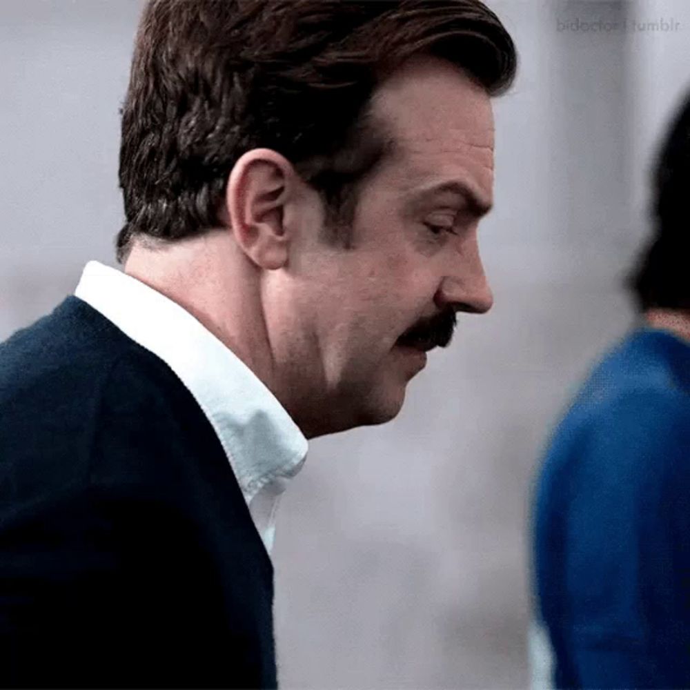 a man with a mustache is wearing a white shirt and a blue sweater .