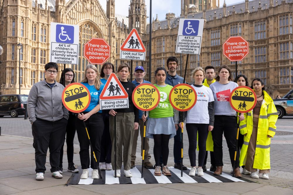 People standing outside parliament with road sign placards with messages like 'stop child poverty going up', 'look out for children'. 