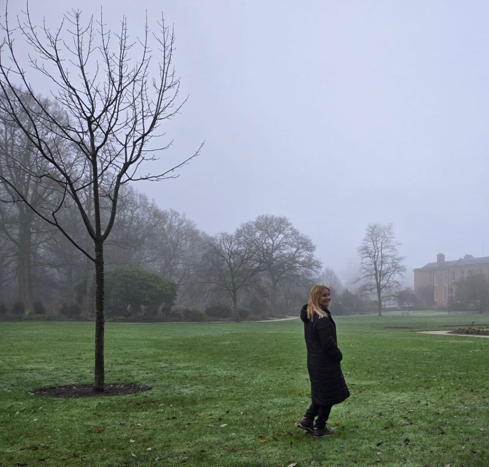 Georgina in a back coat walking across some grass in the fog