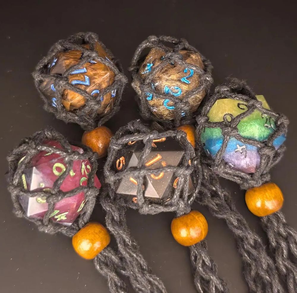 Different colored necklaces made of cord and 20 sided dice in a cage. Colors include but not limited to Gold, Black, Pink and one with a rainbow design