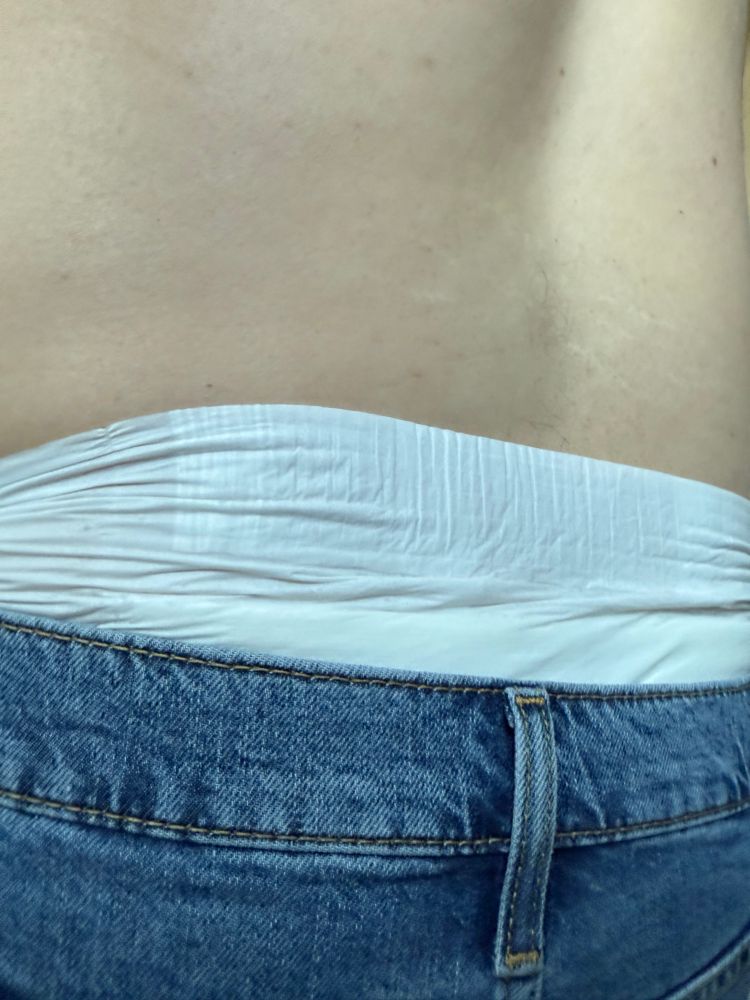 The waist band of a plain white diaper peeking out above denim shorts. 