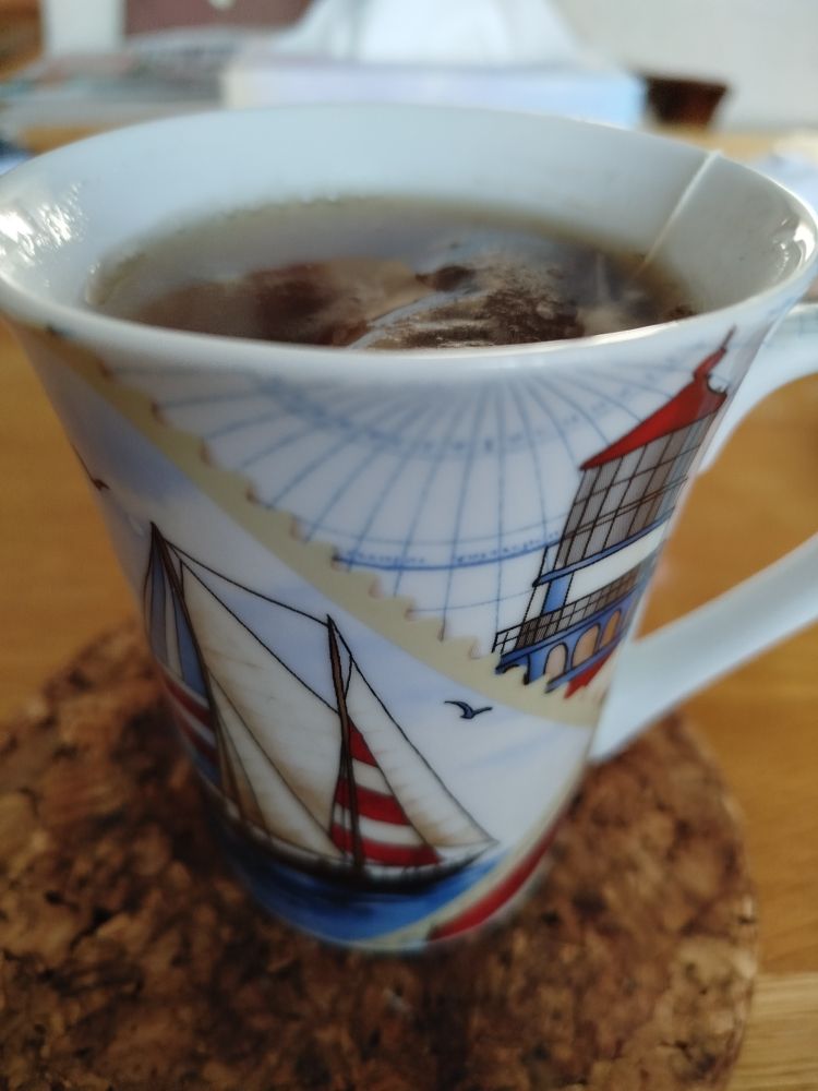 Ein maritim bedruckter Becher, gefüllt mit heißem Wasser und einem Teebeutel 