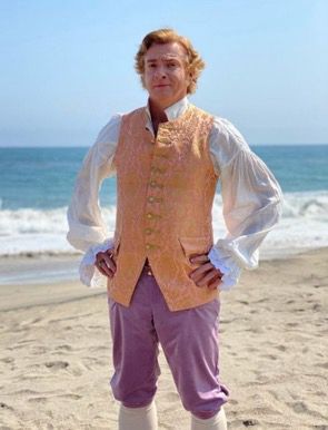 Rhysie looking like a party ring, standing on the beach in his costume from S1E2