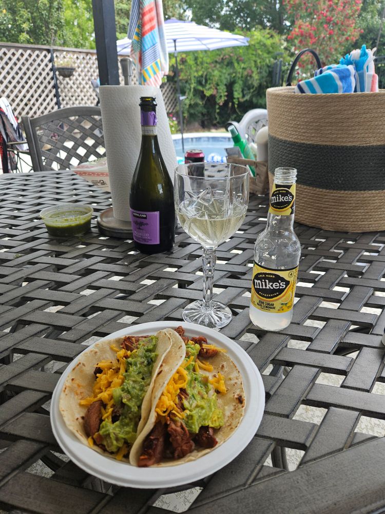 a plate of fajitas, a bottle of Mike's hard lemonade, a bottle and glass of wine, on a table, swimming pool in the background