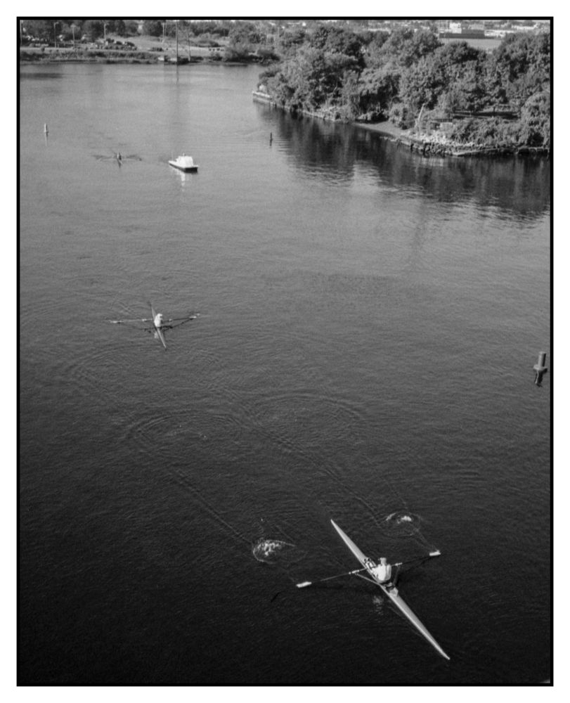Four single sculls and a coach in a bright white launch chase boat on the seekonk River