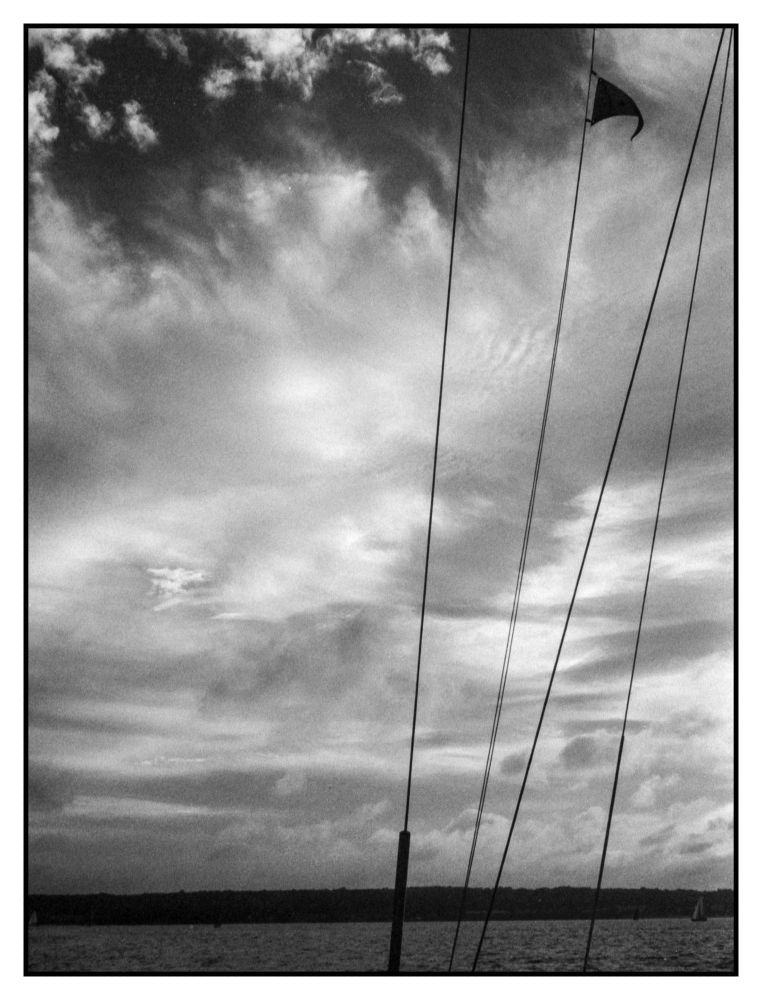 Not a clear sky anymore. Clouds with a small bit of sky near the top and the stays from the mast and a club pennant flying from one of them and the shoreline at the bottom