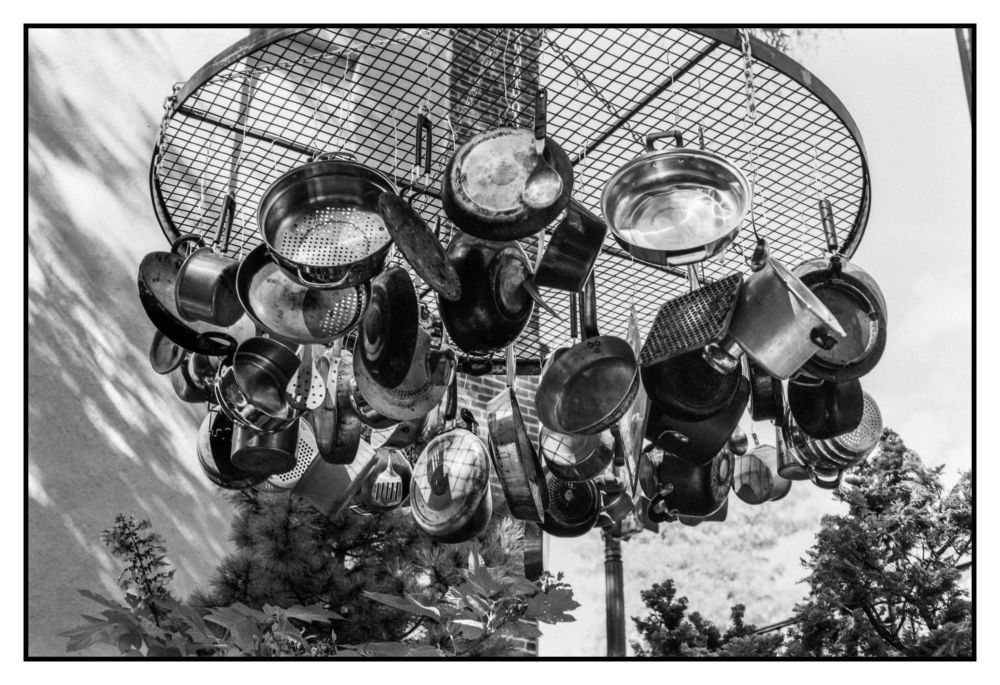 a collection of low quality and used old pots hanging from a circular grill like structure, suspended from a tree outside of the RISD museum