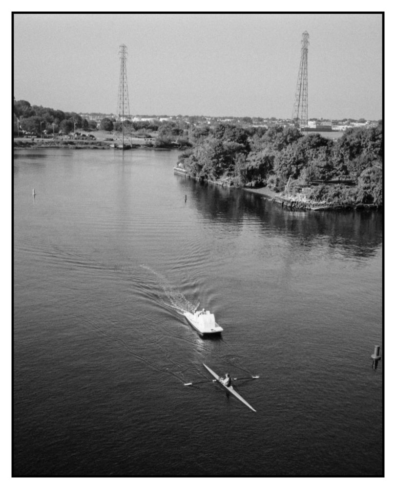 The last rower to start to go under the bridge with the coach following close behind