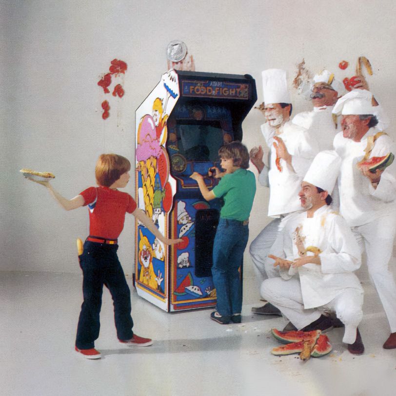 Photo of kid playing the arcade game food fight with a kid about to throw a pie at bunch of chefs who are have already been hit with pies.
