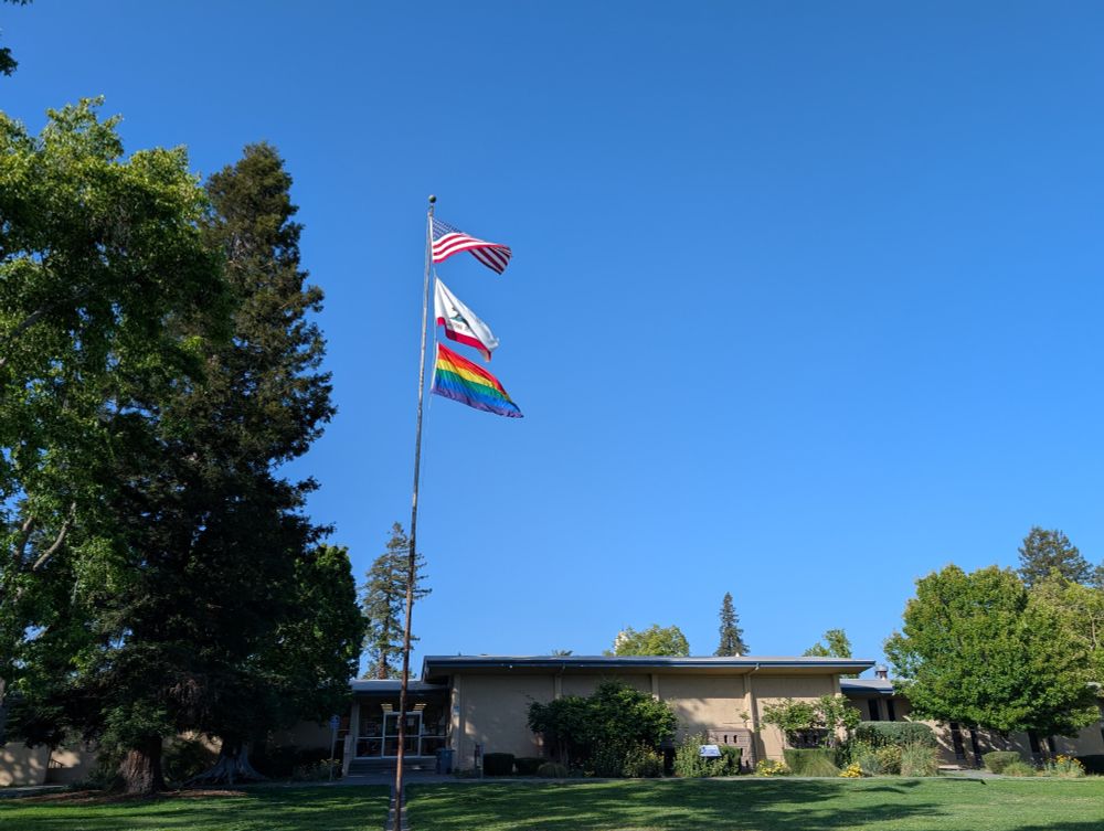 A photo of Petaluma City Hall and the flag pole with US, California, and Pride flags waving in the wind.