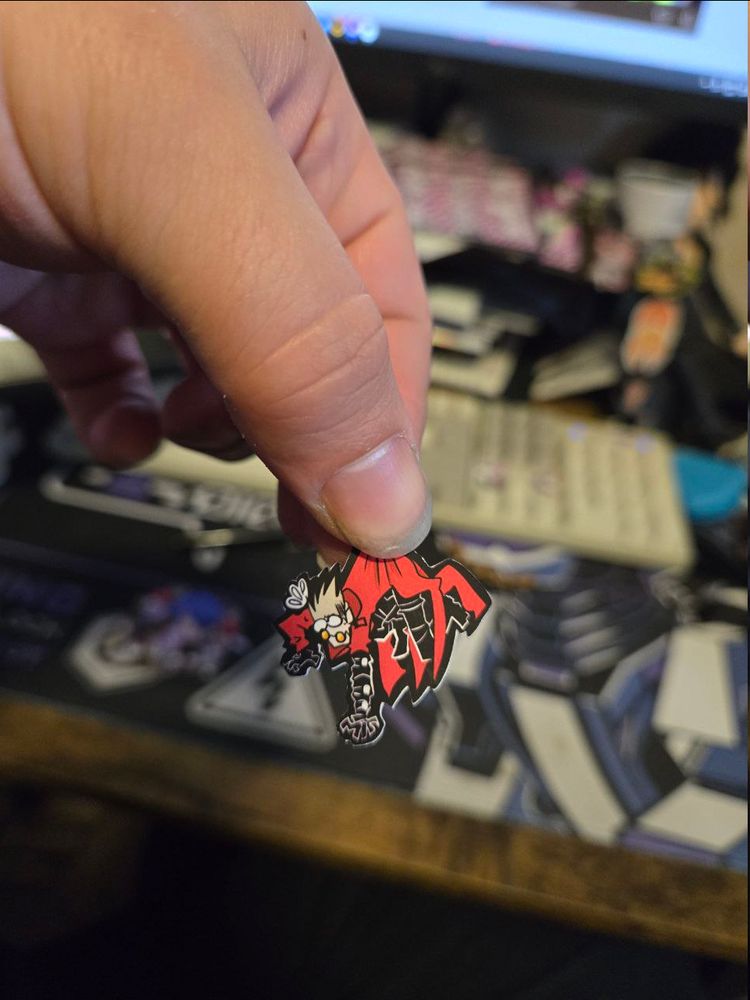 a small sticker of vash is being held up to the camera, the art makes him appear as though he is actually being held and panicking about it
