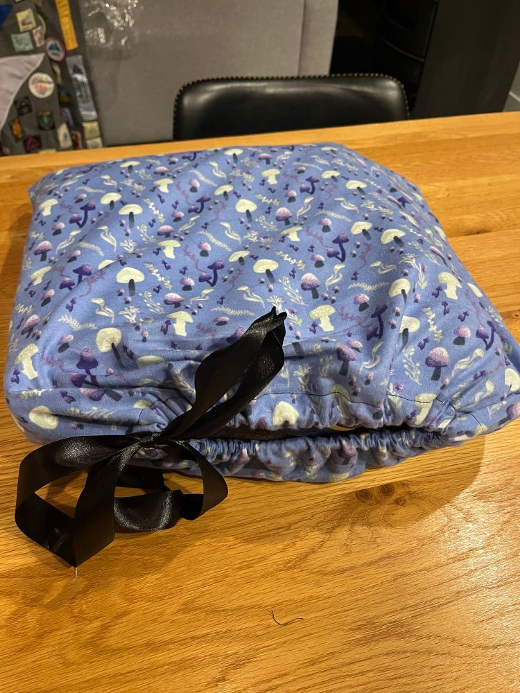 A drawstring bag made from the same purple fairy mushroom fabric with black ribbon