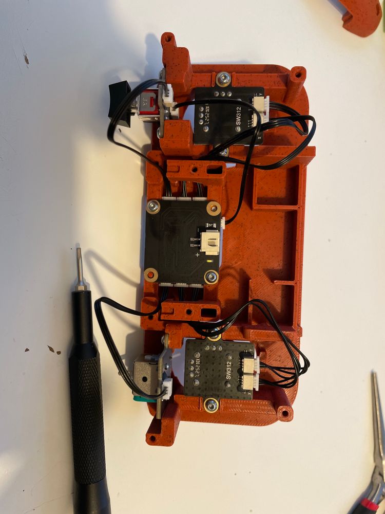 Cyberbrick controller electronics partially assembled. There’s a transmitter in the middle, 2 xy joysticks, a single axis stick, a button and a 3 way toggle switch here.