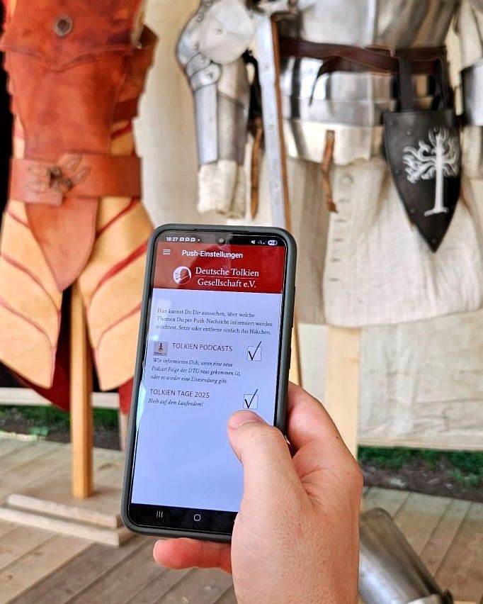 eine Person hält ein Telefon vor einer Metallrüstung