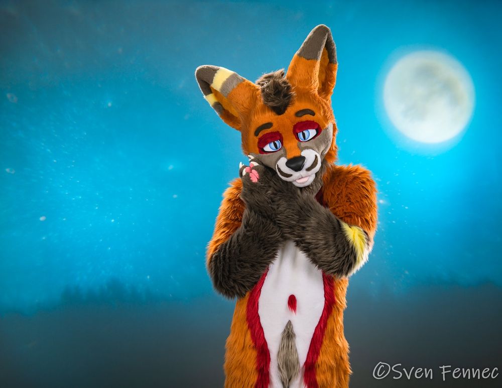 A photo of Sven in their studio with practical backlighting gel of a moon and night skyline with a shadowed tree-line. 
