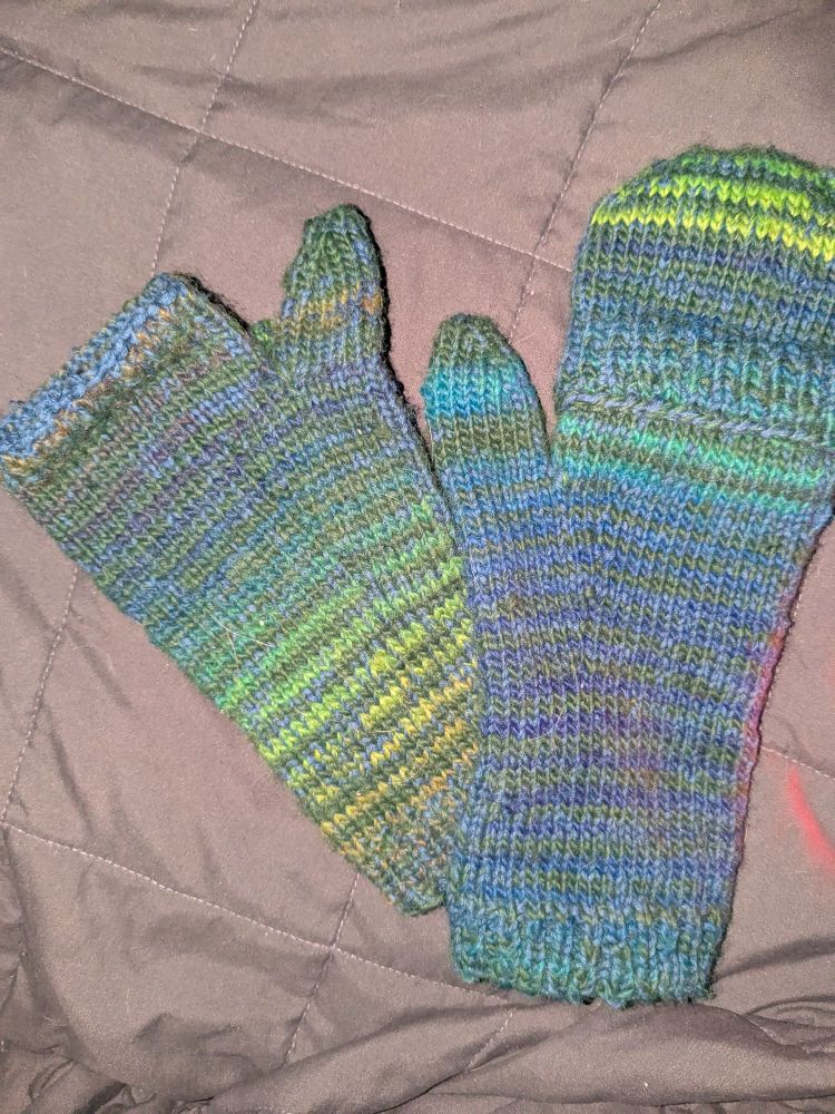 Two mittens in greens and blues on a grey background. One has a cover, one is fingerless
