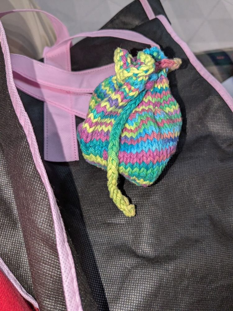 Small knit rainbow cotton money bag, tied closed.