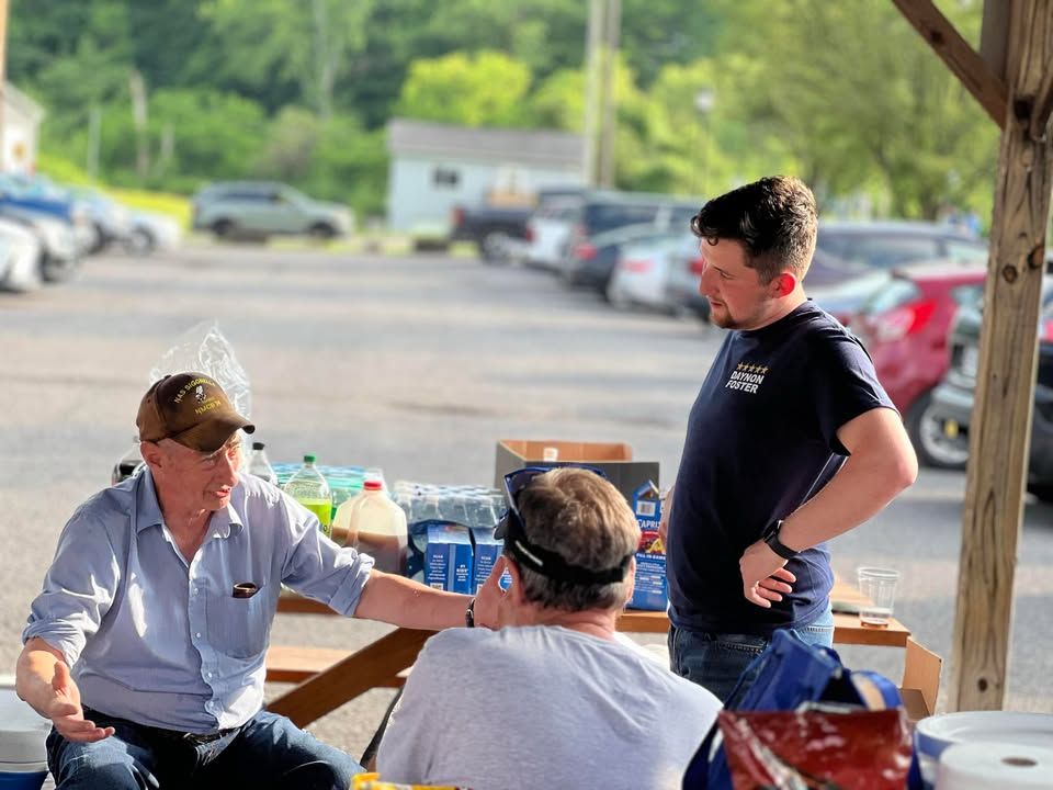 Three men have a discussion at a picnic table.