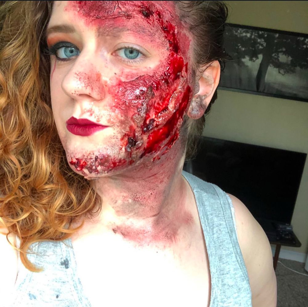 Women with blonde hair looking slightly to left, side of face has fake burns on it. Fake blood and burnt skin