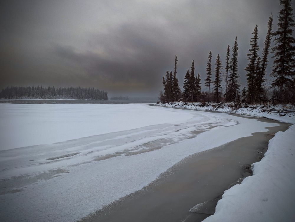 Winter scene with a frozen lake and trees. Dramatic sky.