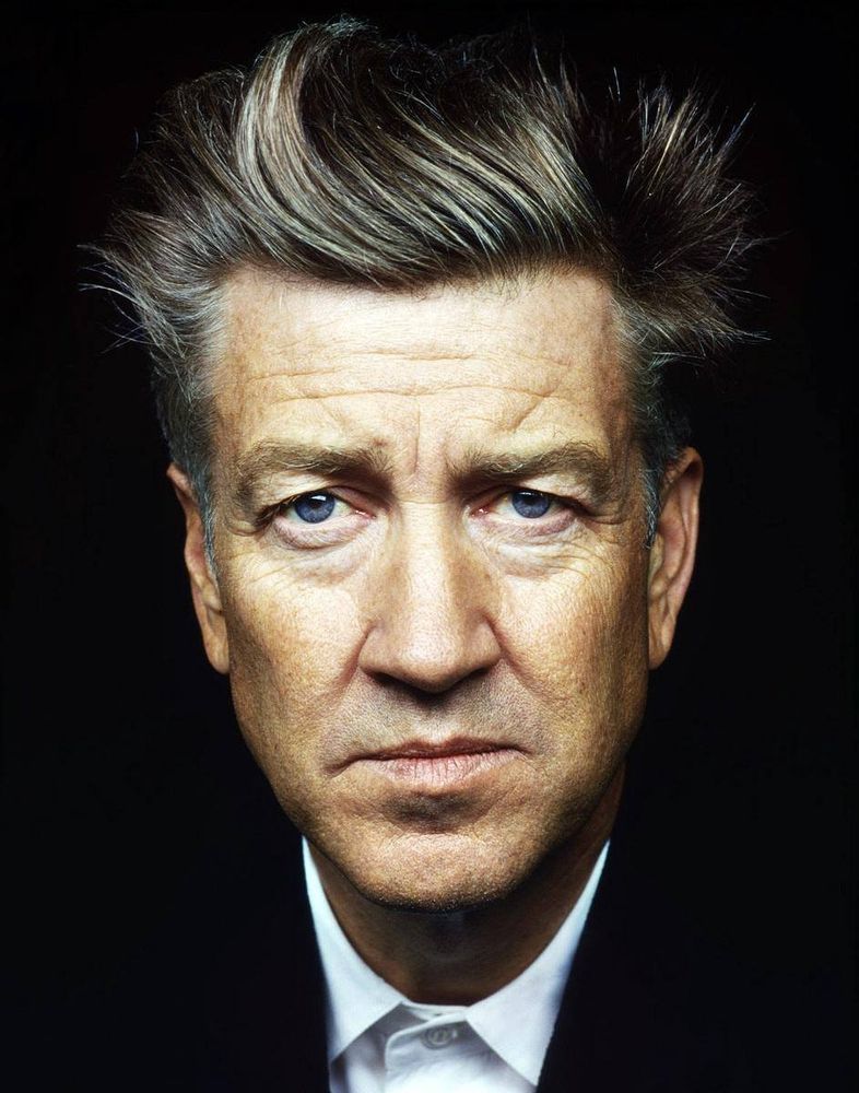 A headshot of director and auteur David Lynch in a black suit with a white shirt