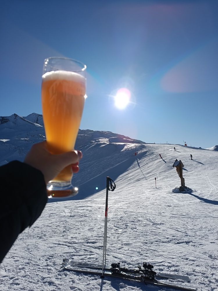 Ein Weizen wird in die Sonne gehalten. Im Hintergrund eine Skipiste bei strahlenden Sonnenschein und blauen Himmel.