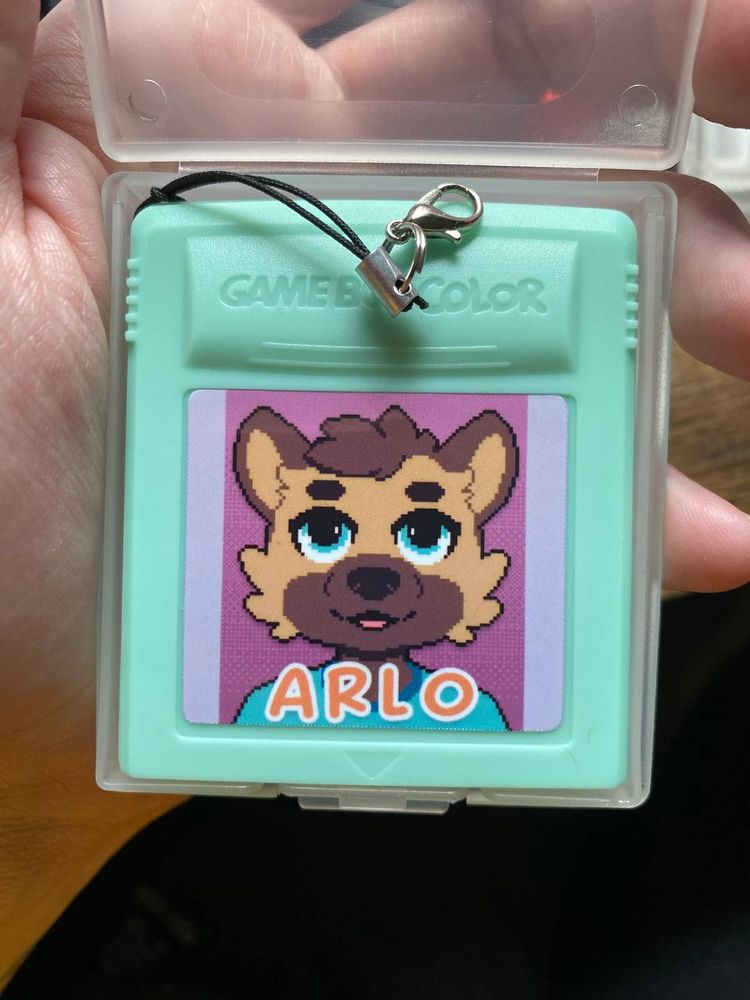 a light sea foam colored game boy color cartridge with an illustration of a german shepard character on a purple background with text on the bottom that reads 'arlo'