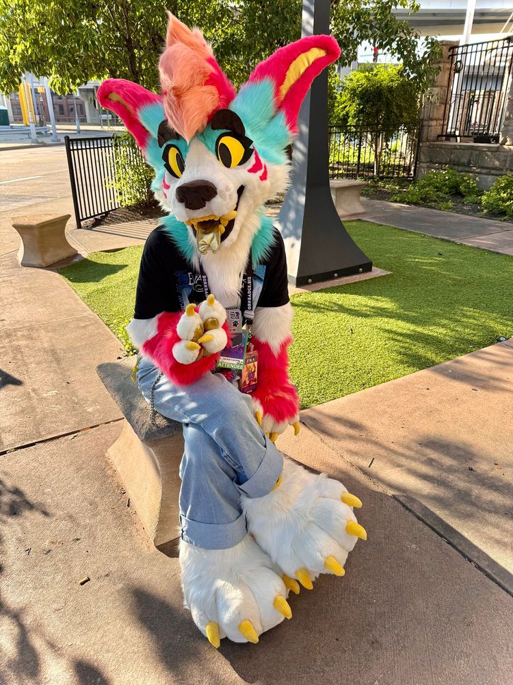 A picture of me sitting outside in my Gemini Jackal partial fursuit. I’m holding up a peace sign gesture with my hand paw.