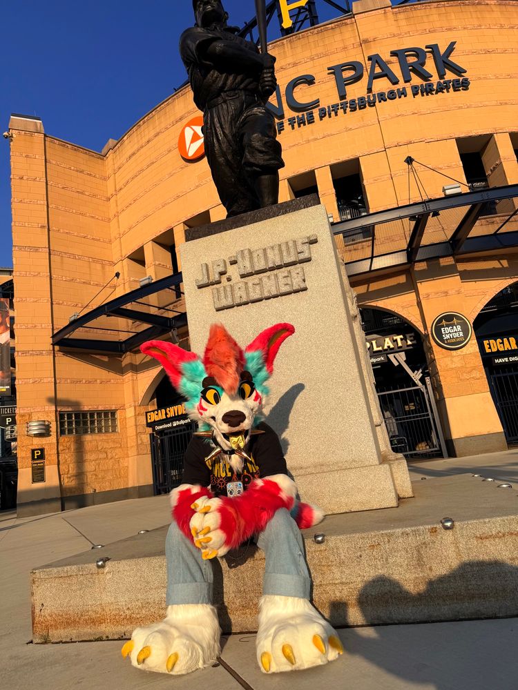 A picture of me sitting outside wearing my Gemini Jackal partial fursuit in front of the PNC Park baseball stadium.