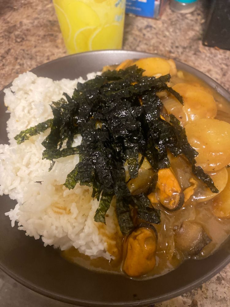 A bowl of white rice and japanese curry with mussels, potato, onion, and mushrooms with seaweed sprinkled on top. 