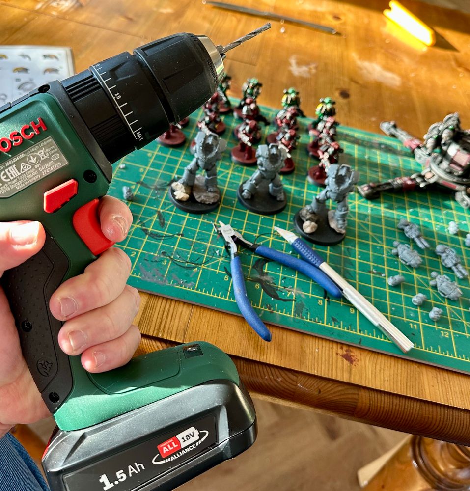 A craft mat with some half-built Warhammer miniatures, a set of clippers, a craft knife, and a power drill. 