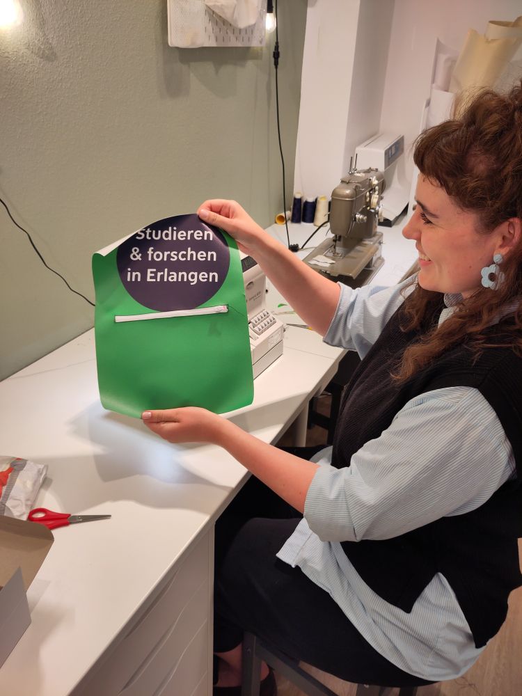 Eine lächelnde Frau hält ein Stück Material, in dem ein Reißverschluss eingenäht wurde, hoch.