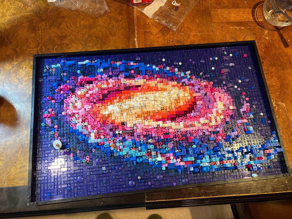 Photo of a completed Lego Milky Way galaxy kit, sitting on a brown wood table. 